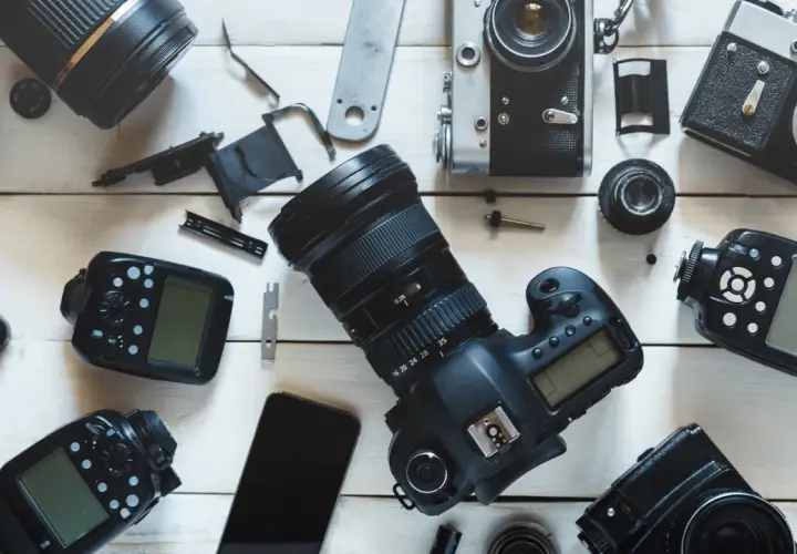 Rozłożone na białym tle aparaty fotograficzne, obiektywy i lampy błyskowe.