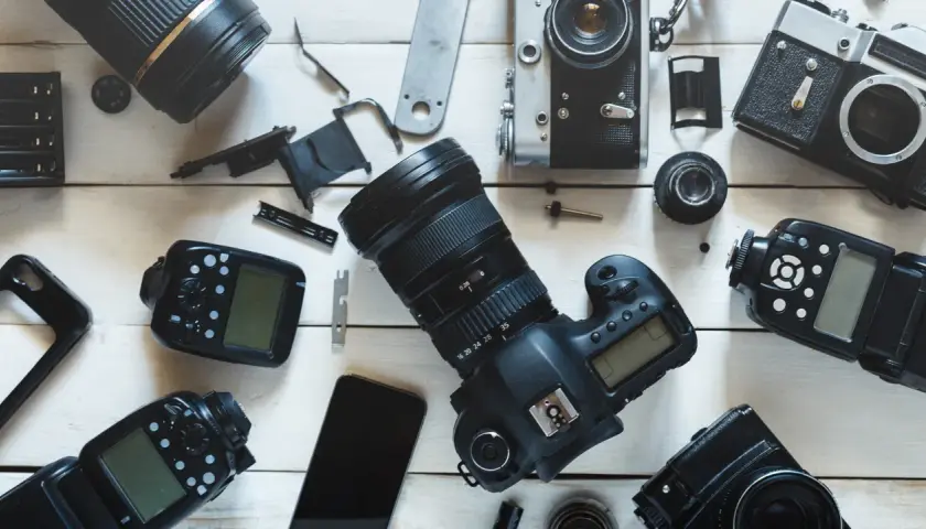 Rozłożone na białym tle aparaty fotograficzne, obiektywy i lampy błyskowe.